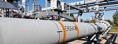 A grey gas pipeline with warning labels and valves at an outdoor industrial facility.