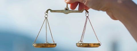 A hand holds a scale. The scale features two bowls suspended by chains.
