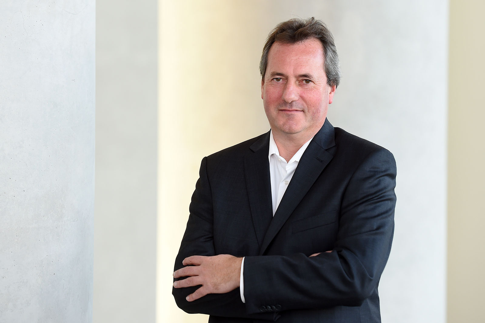 Andreas Frohwein in a grey suit stands in front of a modern building, wearing a white shirt.