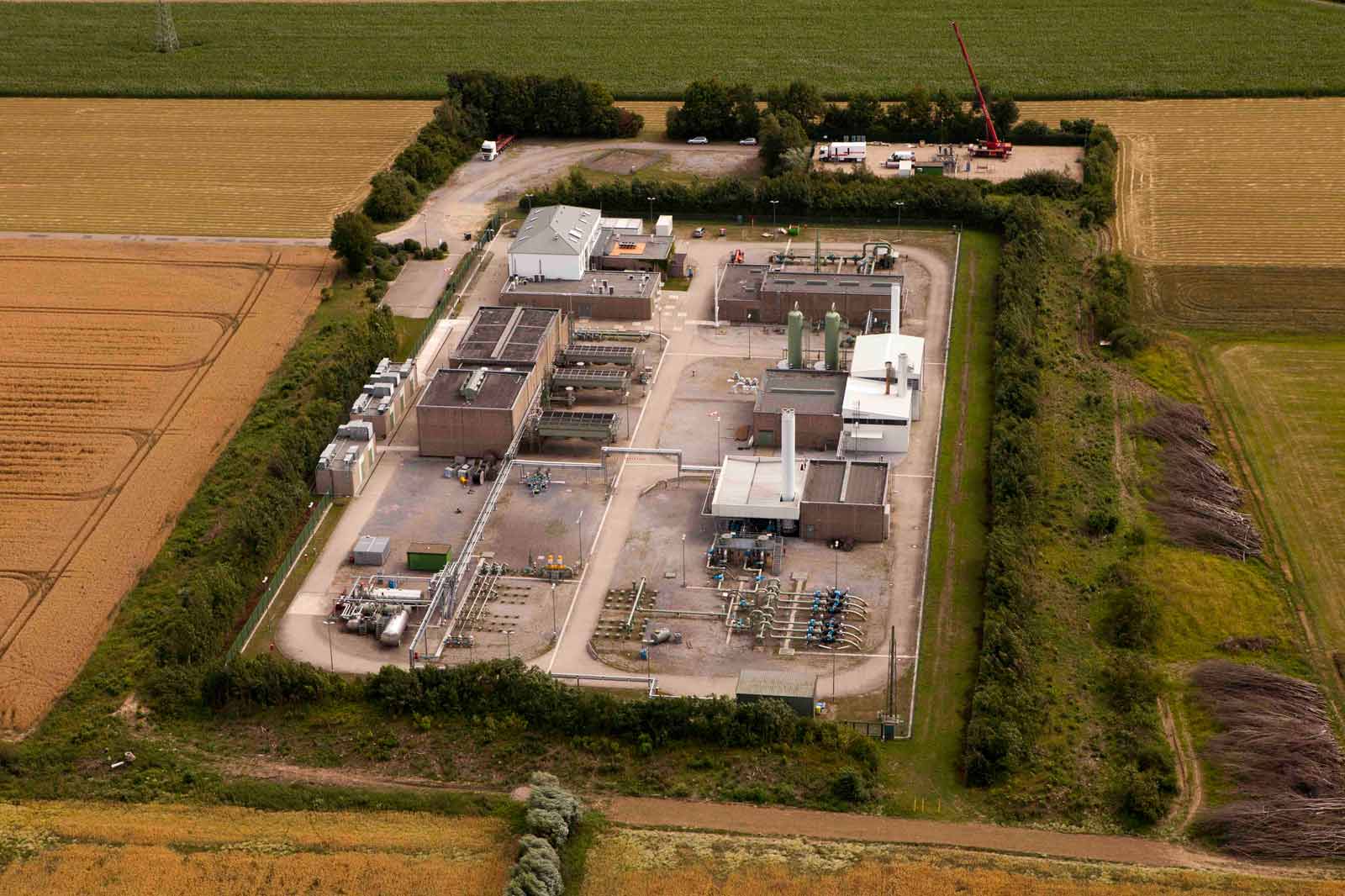 Eine Luftaufnahme einer industriellen Anlage inmitten von Feldern, umgeben von Bäumen und einer Betonfläche mit Geräten.