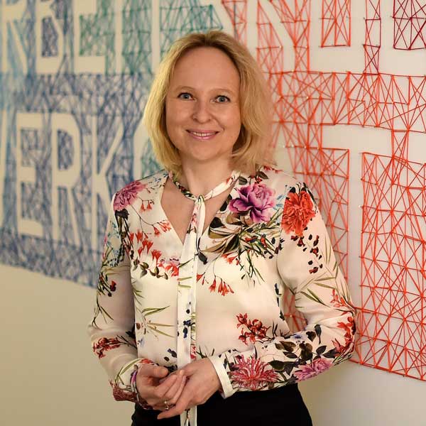 A person is wearing a floral blouse in front of a wall featuring geometric patterns and the word 'NETWORK'.